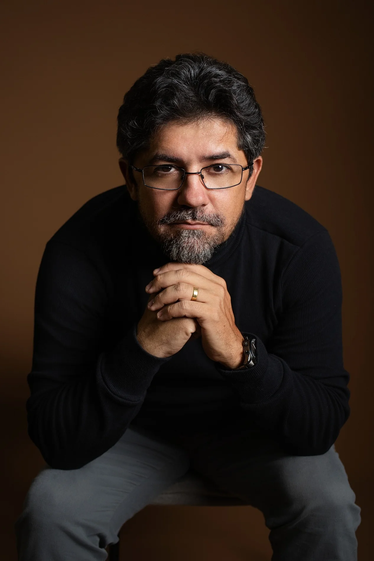 Retrato profissional de Paulo Tozzi, com roupa preta e fundo marrom